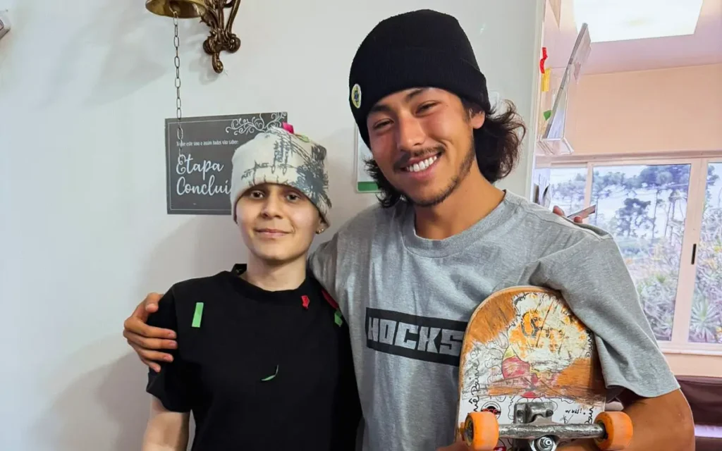 Jovem em remissão do sarcoma de Ewing abraçado a skatista, segurando skate, em ambiente de clínica oncológica em Curitiba